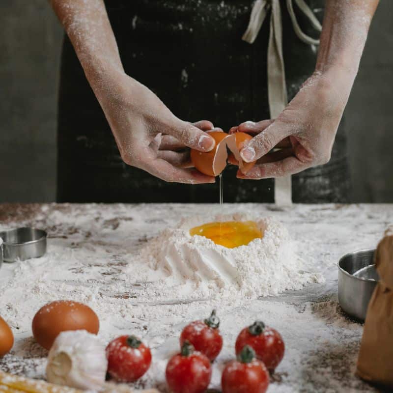 Hands cracking eggs into flour to make traditional Italian egg pasta